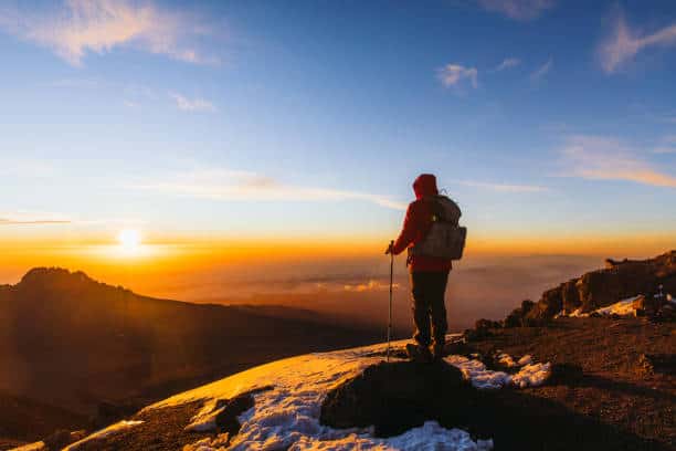 best time to climb Mount Kilimanjaro - Best Time to Climb Mount Kilimanjaro OUR client with backpack and hiking poles got to the top of Africa - Mount Kilimanjaro and looking at the beautiful bright sunny sunrise above the Meru mountain